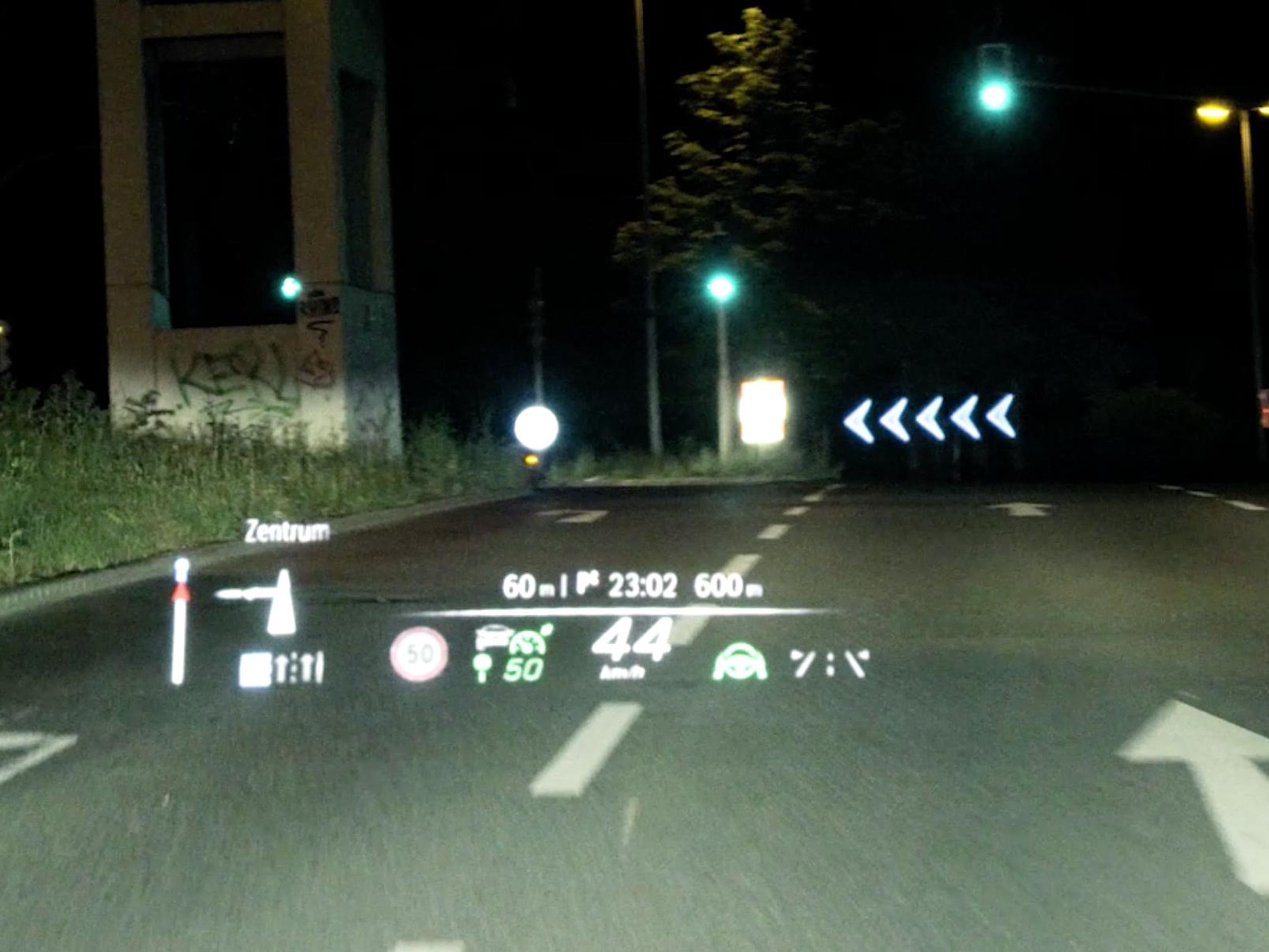 View of an intersection at night. An overlay shows arrows for turning left as well as car and road information.