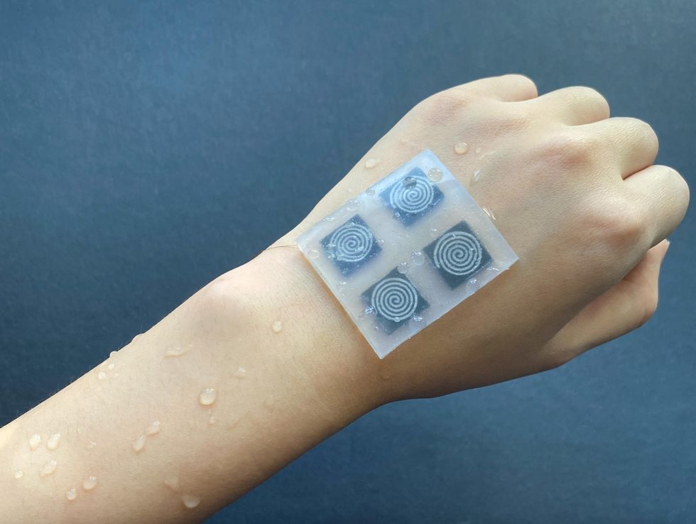 White plastic rectangular patch with four buttons is stuck on the back of a person\u2019s hand. Beads of water on the hand run off the waterproof patch.