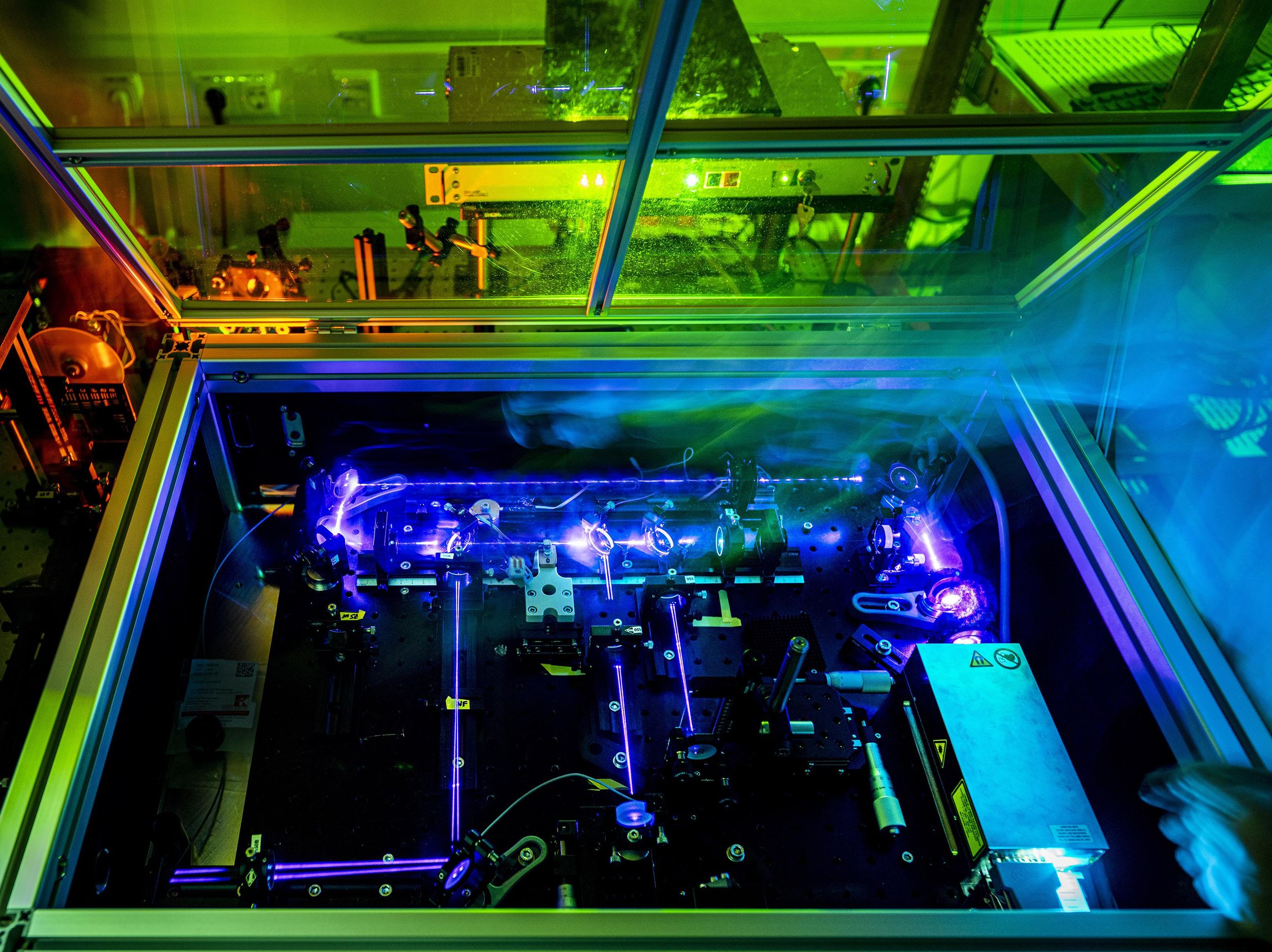 Within an enclosure, violet colored laser beams are visible along with equipment