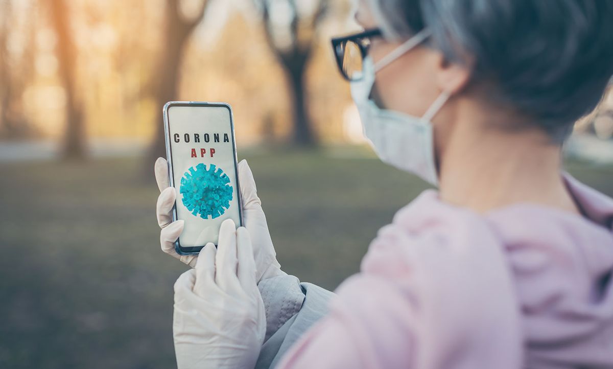 Woman wearing mask and gloves checking a COVID-19 app on her smartphone