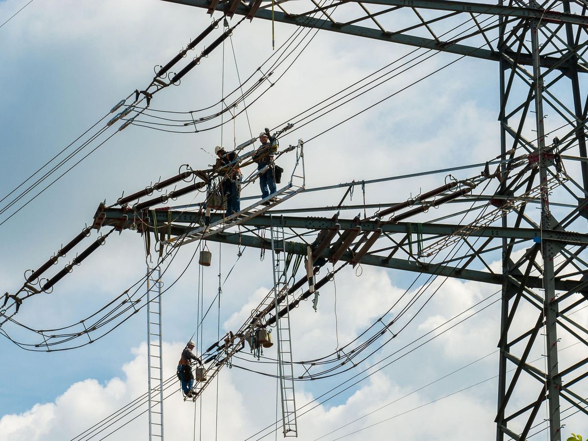 Workers on an electrical line with cloudy sky in background