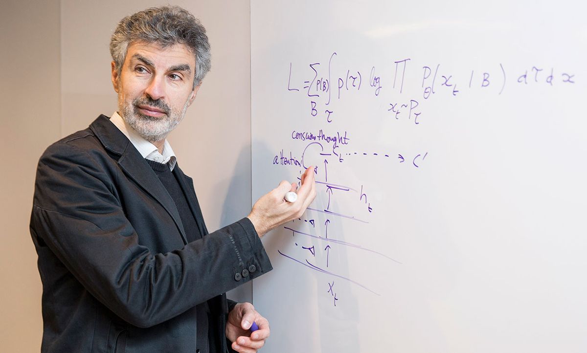 Yoshua Bengio in front of a white board with equations.