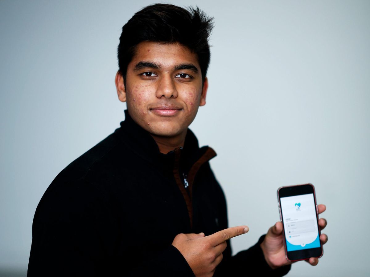 young man posing for a portrait and pointing to a smartphone on a light background